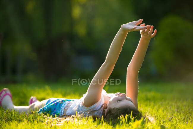 Девочка лежит на траве с поднятыми руками — стоковое фото