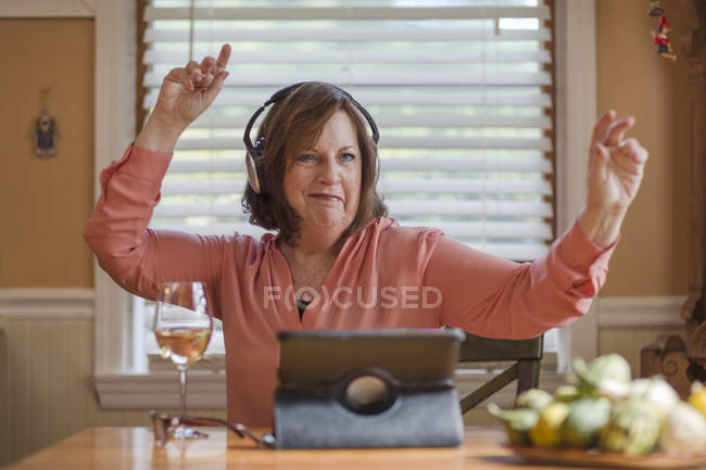 Старша жінка за кухонним столом слухає і танцює на навушники — стокове фото