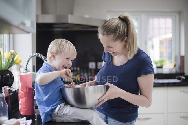 Madre e hijo jugueteando mientras hornean, revolviendo la mezcla en el tazón de mezcla - foto de stock