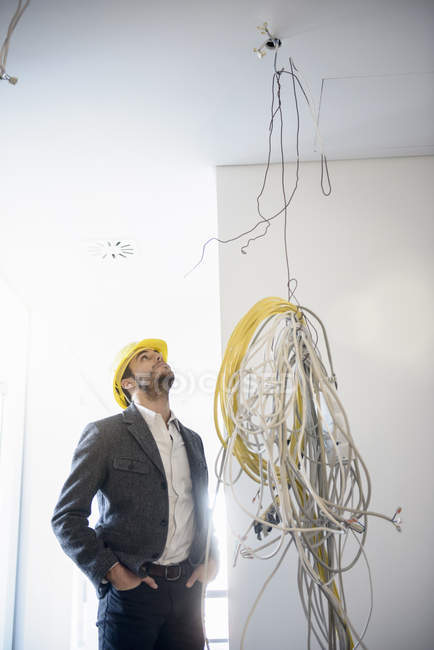 Homme d'affaires regardant vers le haut des câbles suspendus au nouveau plafond de bureau — Photo de stock