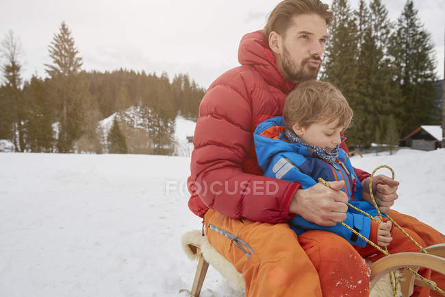 Молодой человек и сын катаются на санках по снегу, Эльмау, Бавария, Германия — стоковое фото