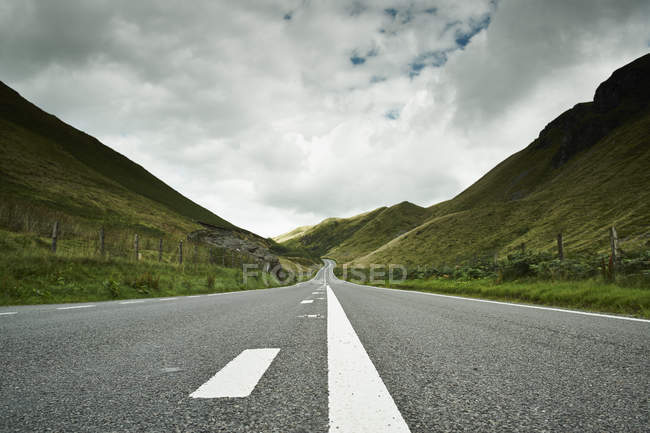 Estrada que se estende através de colinas verdes sob céu nublado — Fotografia de Stock