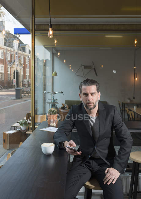 Retrato de empresário legal sentado no assento da janela do café com smartphone — Fotografia de Stock