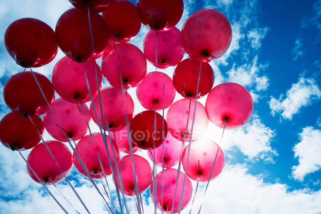 Vue à angle bas de ballons rouge vif contre le ciel bleu — Photo de stock
