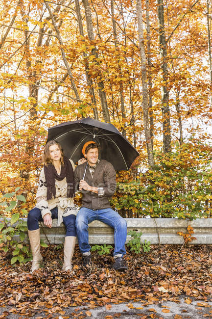 Пара сидить на паркані з парасолькою — стокове фото