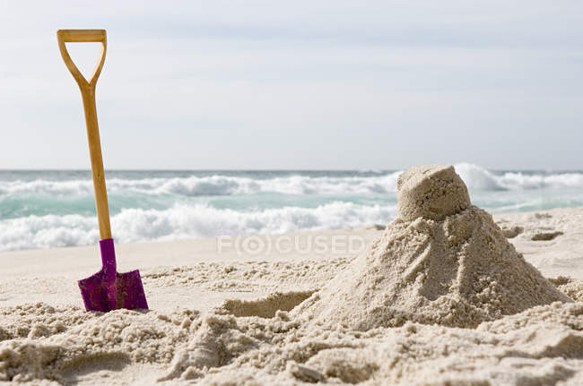 Spade and sandcastle on beach — Stock Photo