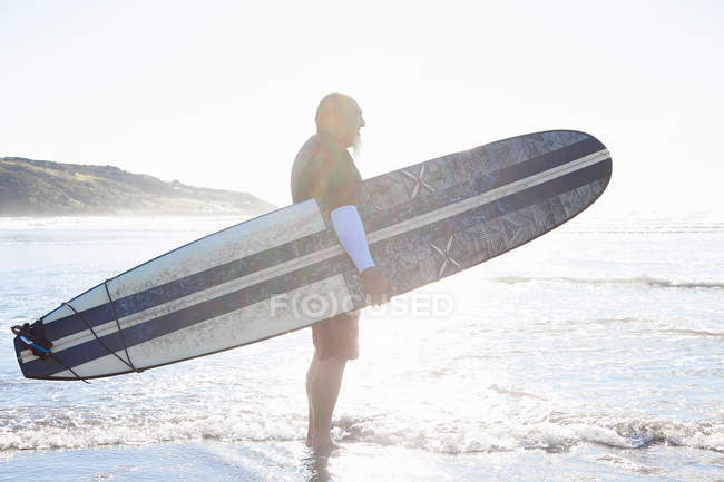 Зрелый серфер наблюдает за морем с пляжа — стоковое фото