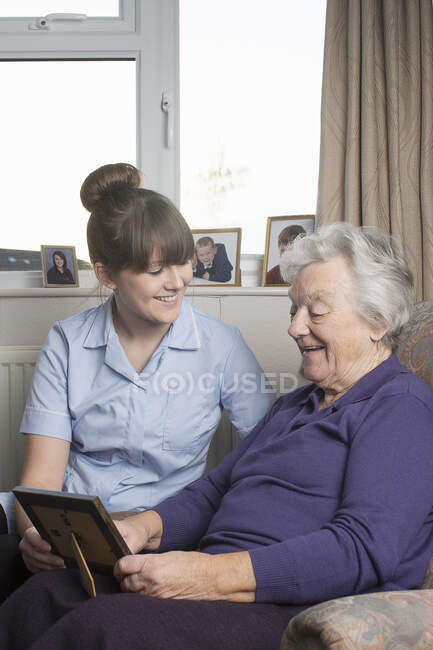 Assistente de cuidados pessoais olhando para a fotografia com a mulher idosa — Fotografia de Stock