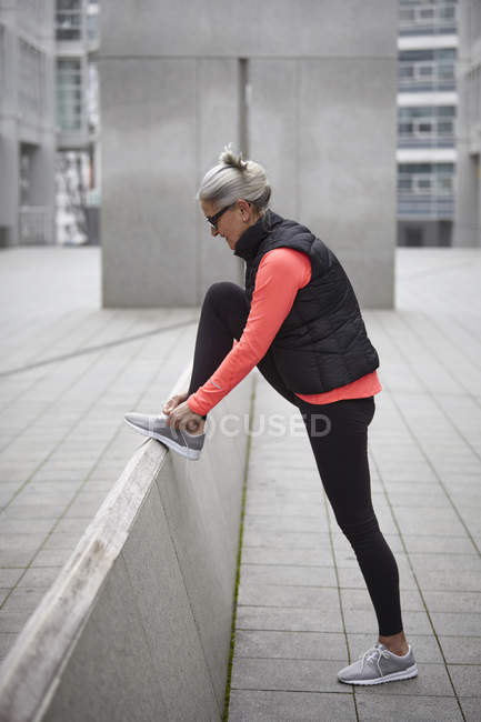 Зріла жінка тренується в місті, зав'язуючи тренерів мереживами — стокове фото