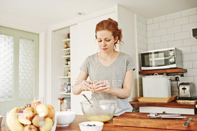 Mitte erwachsene Frau knackt Eier an Küchentheke — Stockfoto