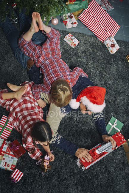 Padre acostado en el piso de la sala de estar abriendo regalos de Navidad con hija e hijo — Stock Photo