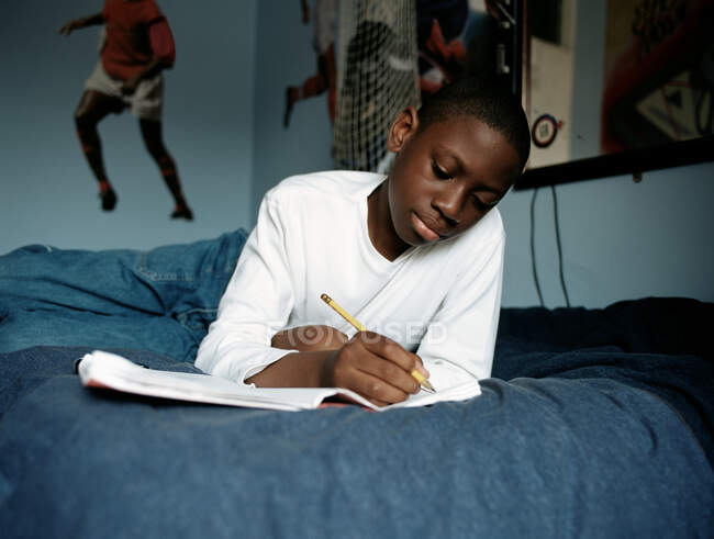 Junge macht Hausaufgaben im Bett — Stockfoto