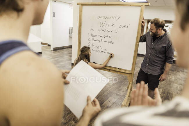 Teenage girl writing list on whiteboard in front of high school class — Stock Photo