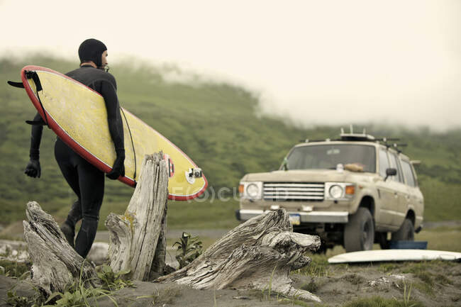 Homem carregando prancha de surf em direção ao carro, Kodiak, Alaska, EUA — Fotografia de Stock