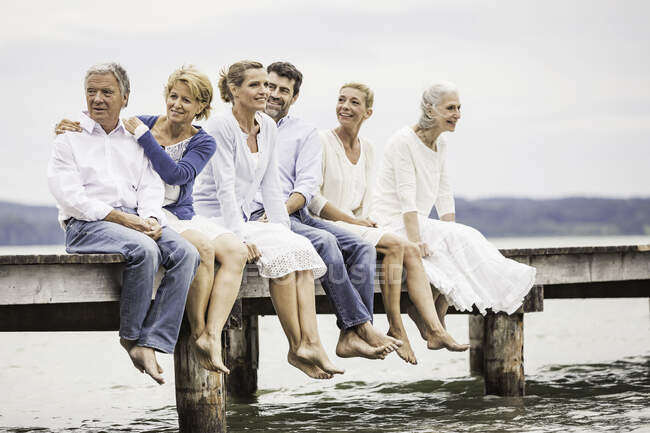 Group of friends, sitting in row on edge of pier — Stock Photo