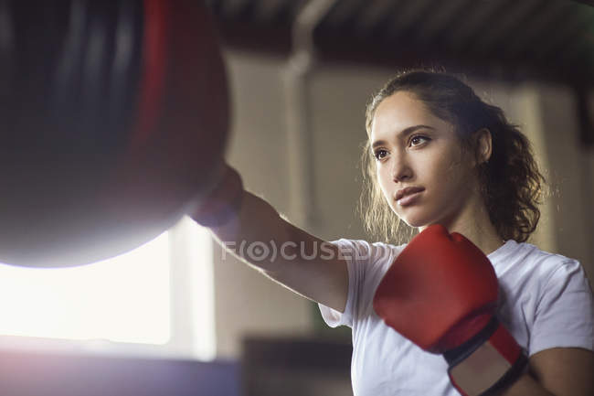 Jovem boxeador feminino perfurando saco de soco no ginásio — Fotografia de Stock