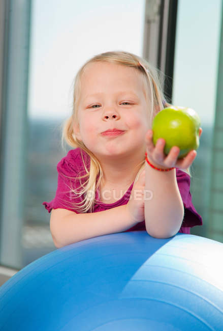 Дівчина їсть яблуко на тренувальному м'ячі — стокове фото