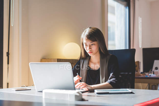 Joven empresaria en el escritorio de la oficina escribiendo en el ordenador portátil - foto de stock