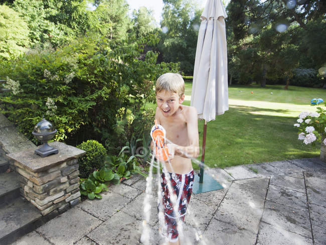Boy squirting hose with water, looking in camera — Stock Photo