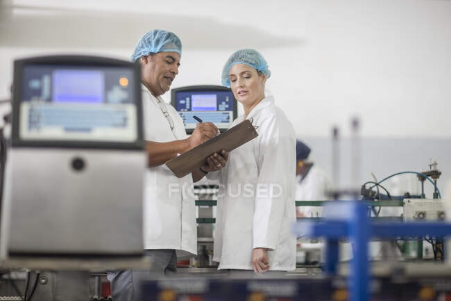 Cape Town, South Africa, male and female staff in packaging factory wearing overalls and safety head nets listing stock itinerary from file — Stock Photo