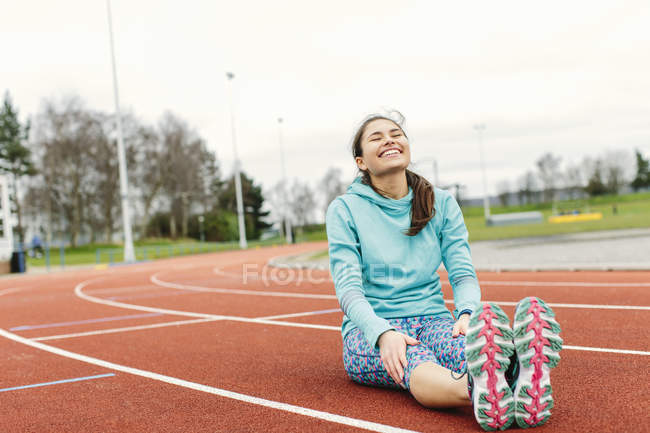 Mujer joven en pista de atletismo, ejercicio, estiramiento - foto de stock