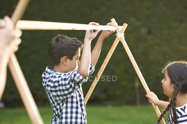 Brother and sister putting up homemade tent frame in garden — Stock Photo