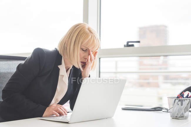 Mujer de negocios madura estresada trabajando en el portátil en el escritorio de la oficina - foto de stock