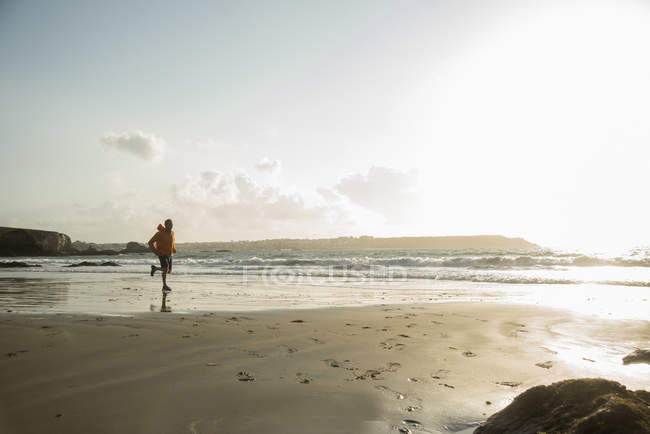 Зрелый человек бежит по песку вдоль береговой линии — стоковое фото