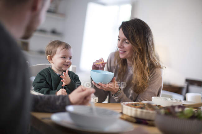 Parents à table à manger nourrissant bébé garçon souriant — Photo de stock