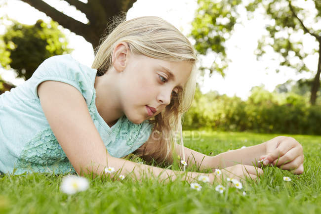 Mädchen liegt auf Gras und starrt Gänseblümchen an — Stockfoto