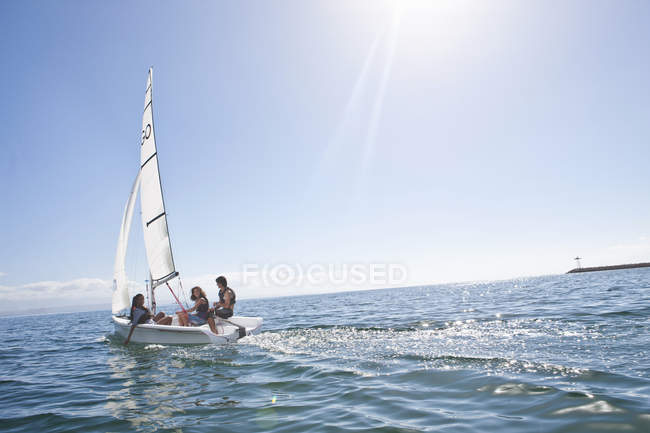 Three young friends sailing out from harbor on water — Stock Photo