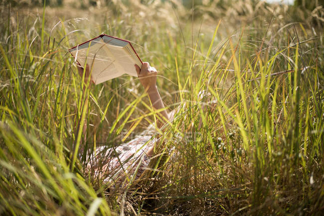 Женщина лежит в длинной траве, читая книгу — стоковое фото