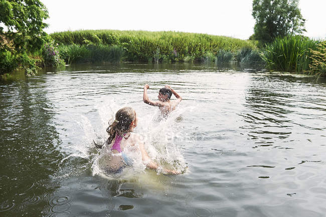 Adolescente menino e irmã espirrando no lago rural — Fotografia de Stock