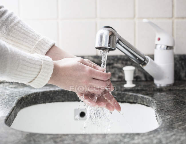 Cortado tiro de mujer joven lavándose las manos en el fregadero - foto de stock