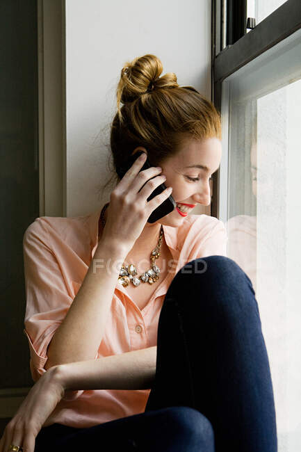 Jeune femme au téléphone, regardant par la fenêtre — Photo de stock