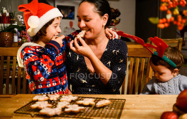 Mãe e dois filhos à mesa comendo biscoitos caseiros de Natal — Fotografia de Stock