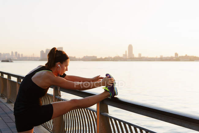 Joven jogger femenino en la orilla del río estiramiento de la pierna - foto de stock