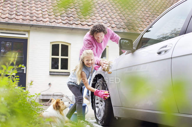 Girl helping father washing car in yard — Stock Photo