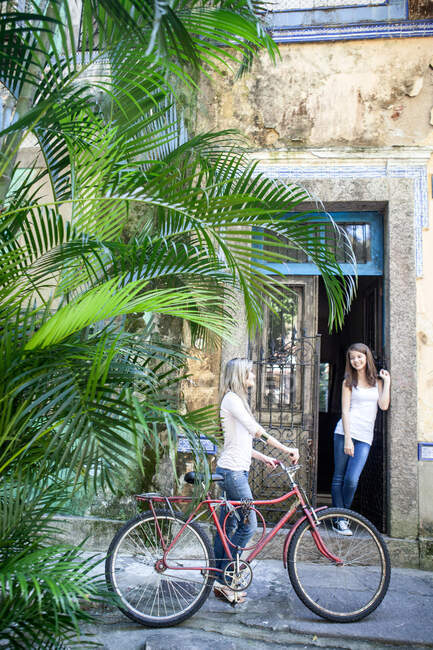 Giovane donna in bicicletta che parla con un amico sulla porta, Rio de Janeiro, Brasile — Foto stock