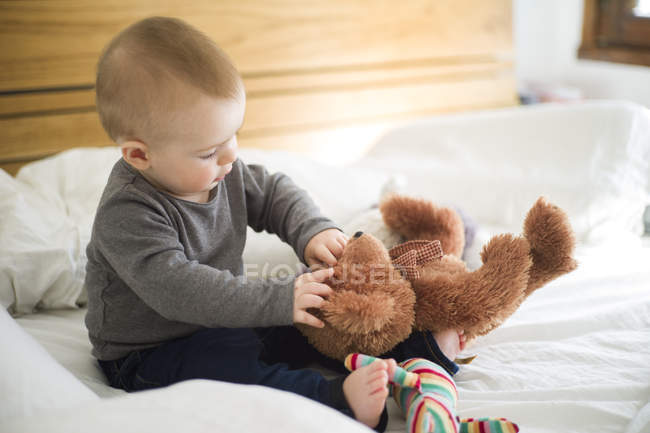 Baby girl sitting on bed playing with teddy bear — Stock Photo