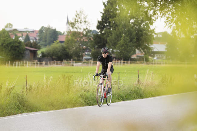 Зрелый мужчина на велосипеде по проселочной дороге — стоковое фото