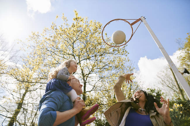 Familia lanzando baloncesto a través de aro de baloncesto - foto de stock