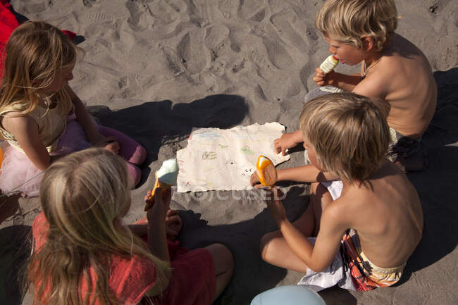 Четверо друзей едят мороженое на пляже под высоким углом, Уэльс, Великобритания — стоковое фото