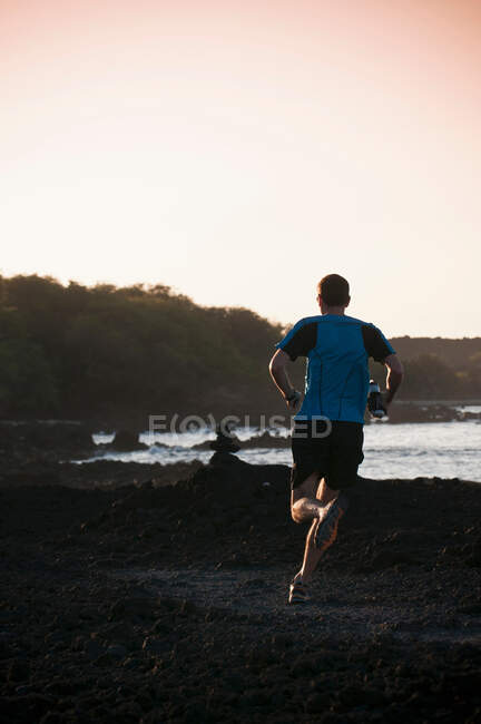 Hombre corriendo en la playa rocosa - foto de stock