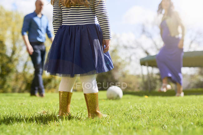 Sección baja de la chica en el jardín con la familia jugando con el fútbol - foto de stock