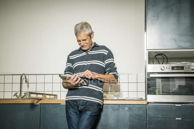 Старший чоловік використовує цифровий планшет на кухні — стокове фото