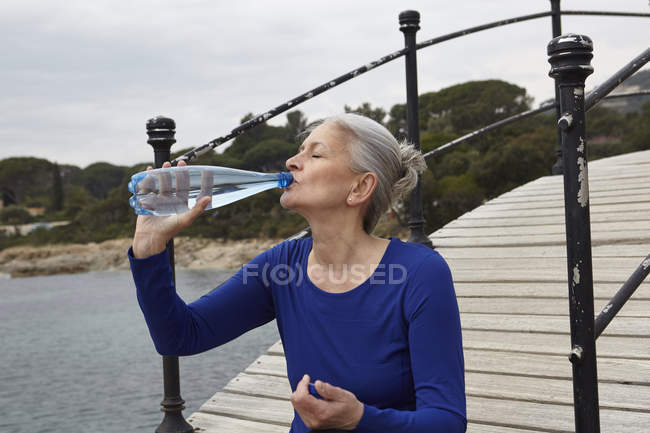 Зрелая женщина на улице, пьет из бутылки с водой — стоковое фото