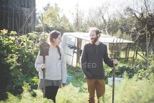 Young couple in garden holding fork and spade — Stock Photo