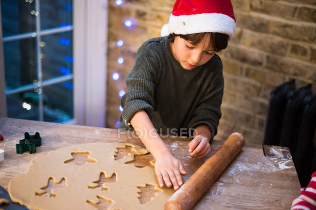 Мальчик в шляпе Санты готовит рождественское печенье на кухне — стоковое фото