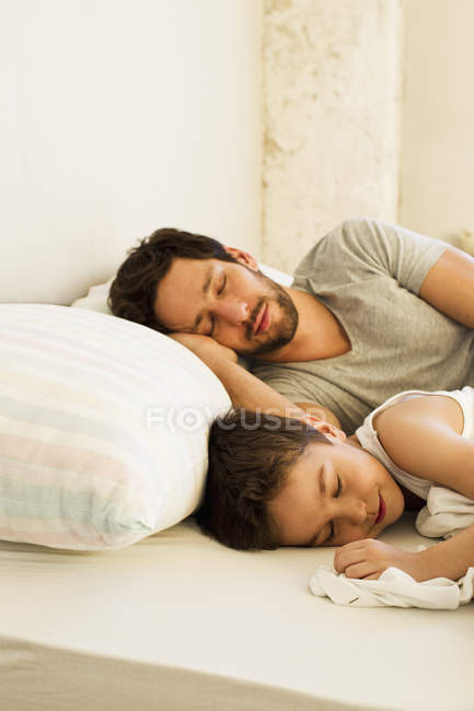 Padre e hijo pequeño durmiendo en la cama en casa - foto de stock